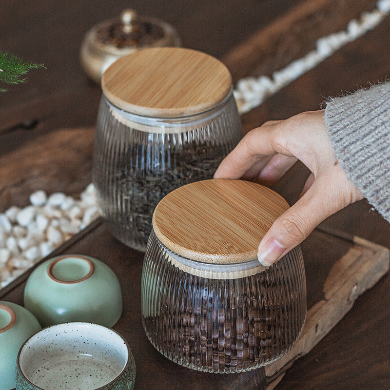 Two ribbed glass tea caddies with loose-leaf tea on a wooden tray