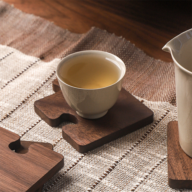 A walnut coaster under a cup of tea on a linen runner